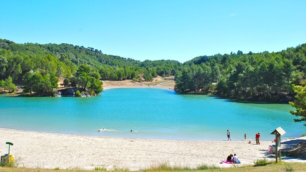 A beach with clear turquoise water, surrounded by forested hills.