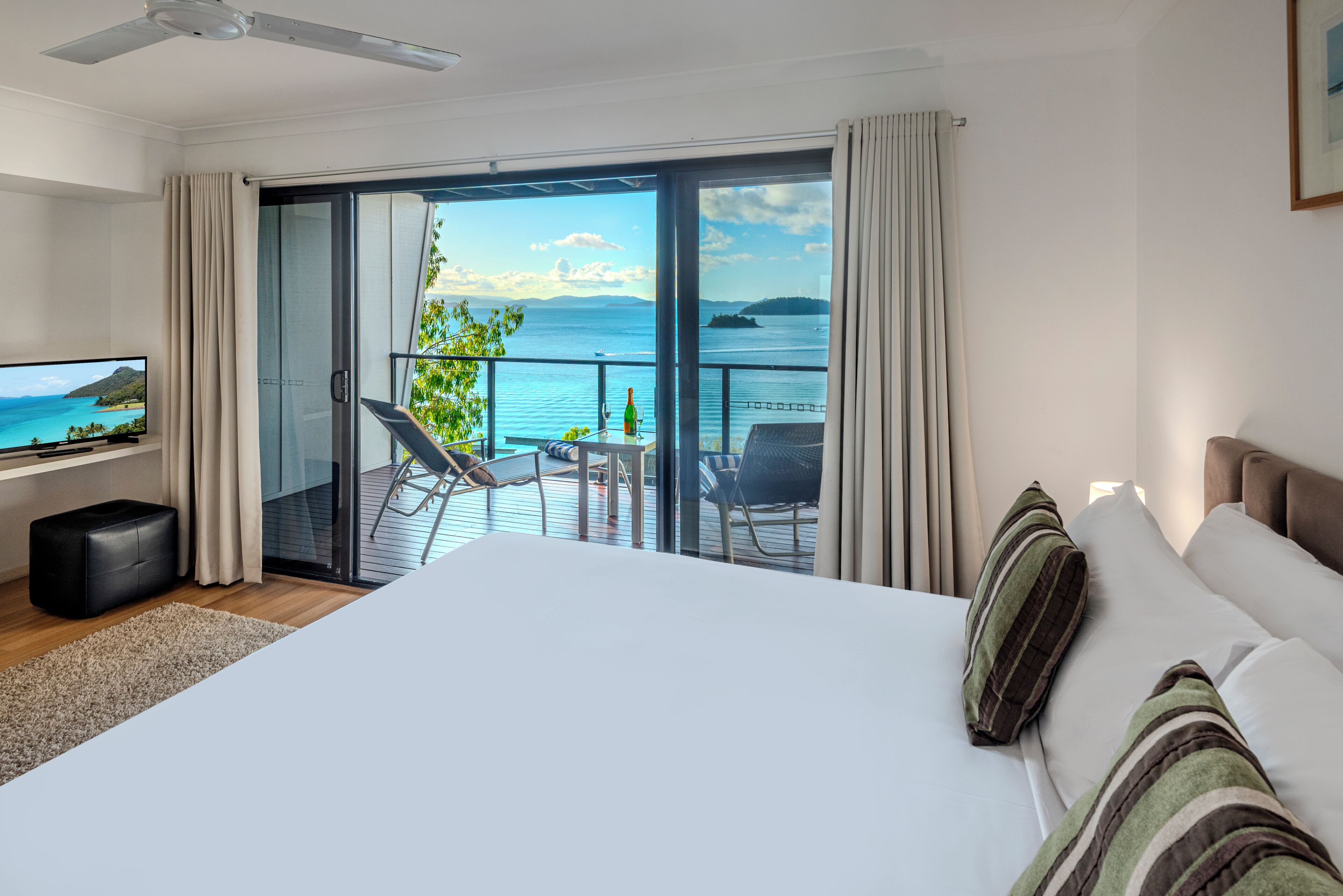 Quarto de hotel com uma cama grande, televisão, varanda com vista para o mar e área de refeições.