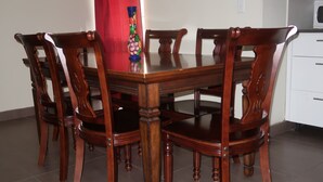 A dining table with six wooden chairs, a vase, and a red curtain. - Two Bedroom two bathroom Apartment A ground level (Willemstad)