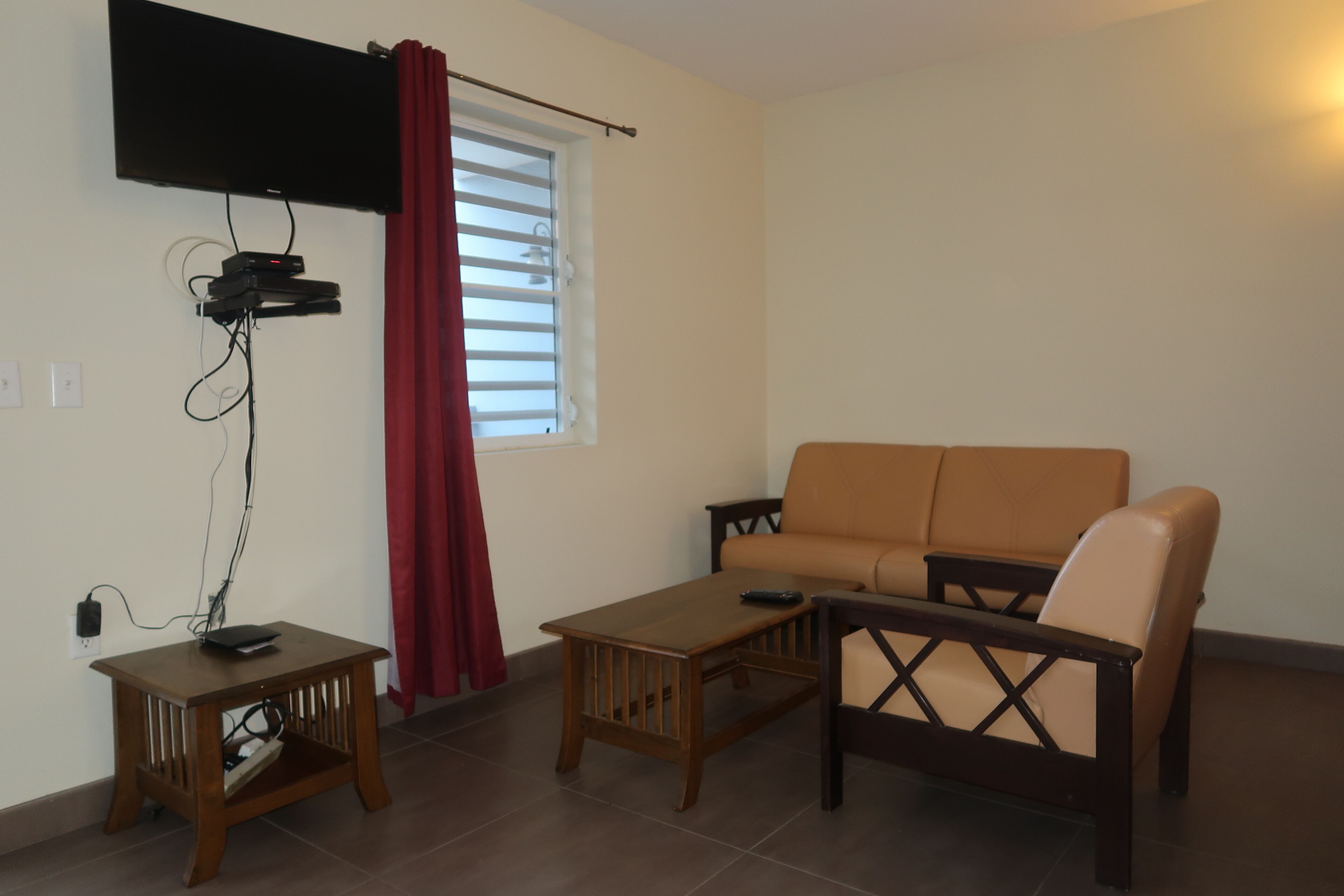 A living room with a sofa, a coffee table, a TV mounted on the wall, and a window with blinds.
