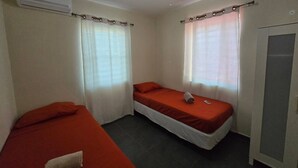 A small, simple room with two single beds, a wardrobe, and an air conditioning unit. - Two Bedroom two bathroom Apartment A ground level (Willemstad)