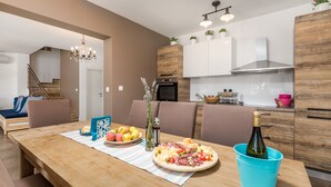 A modern kitchen with wooden cabinets, a dining table set with plates of food, a bottle of wine, and a blue bucket. - Villa Leticia a perfect place for relaxed and complete vacation (Hreljići)