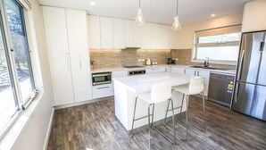 Une cuisine moderne avec des meubles blancs, un grand îlot central doté de tabourets, un réfrigérateur en acier inoxydable et un pare-feu en pierre.
