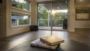 Un intérieur moderne avec de grandes fenêtres, une porte-fenêtre coulissante donnant sur une terrasse, et un livre intitulé « Les plus belles randonnées à vélo du monde » posé sur une table.