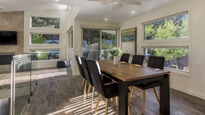Un espace repas moderne avec une table en bois, des chaises noires et une cloison en verre.