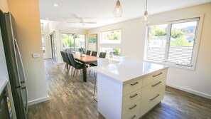 A modern kitchen with a large island, wooden flooring, and large windows offering views of the outdoors.