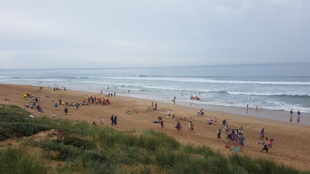Ein Strand mit Menschen, die spazieren gehen und spielen, Zelten und dem Meer im Hintergrund.