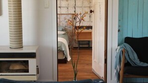 Ein Wohnzimmer mit einer Couch, einem Kamin und Blick in einen weiteren Raum mit einem Bett und einer Pflanze.