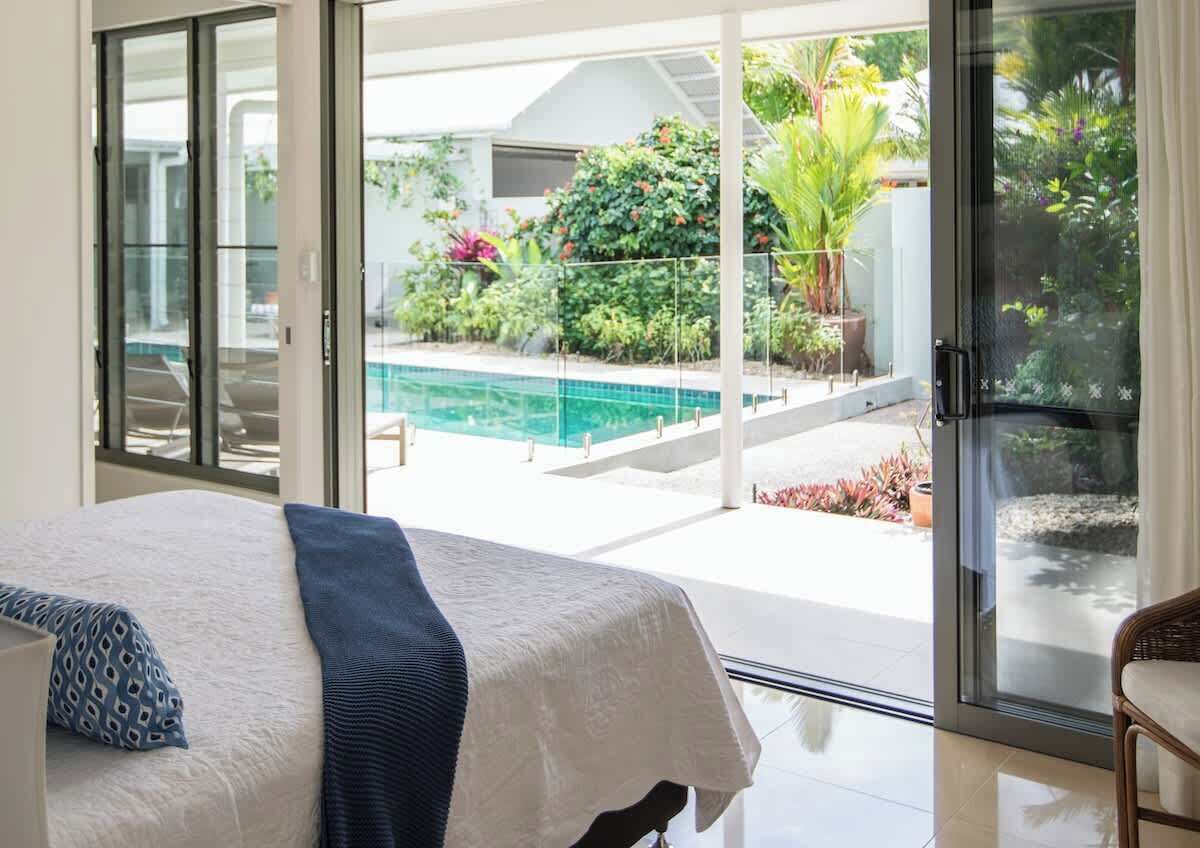 A bedroom with a bed, a view of a swimming pool, and a glass door leading outside.