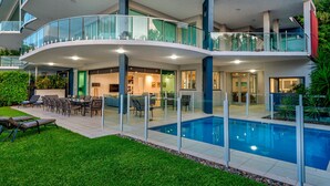 Una casa moderna de varios pisos con piscina, mobiliario exterior y barandillas de vidrio.