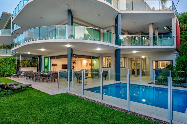 Ein modernes Mehrfamilienhaus mit Schwimmbad, Sitzgelegenheiten im Freien und Glasgeländern.