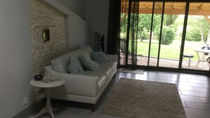 Un salon avec un canapé blanc, une petite table d’appoint, une grande fenêtre donnant sur un paysage verdoyant et un luminaire au plafond.