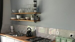 Une cuisine dotée d’un plan de travail en bois, d’une cuisinière à gaz, d’un four encastré et d’une étagère au-dessus de l’évier où sont rangés la verrerie et la vaisselle.
