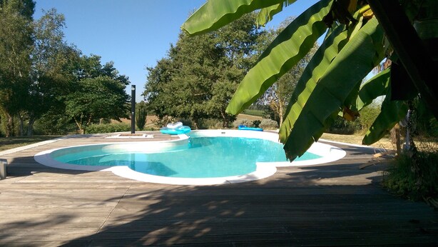 Une piscine entourée d’une terrasse en bois, des arbres en arrière-plan et un ciel dégagé.