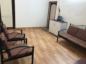 Una stanza con pavimento in legno, un divano, due poltrone, un armadio e una porta.