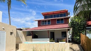 Una casa de dos pisos con piscina, un patio cubierto y un césped cuidado.