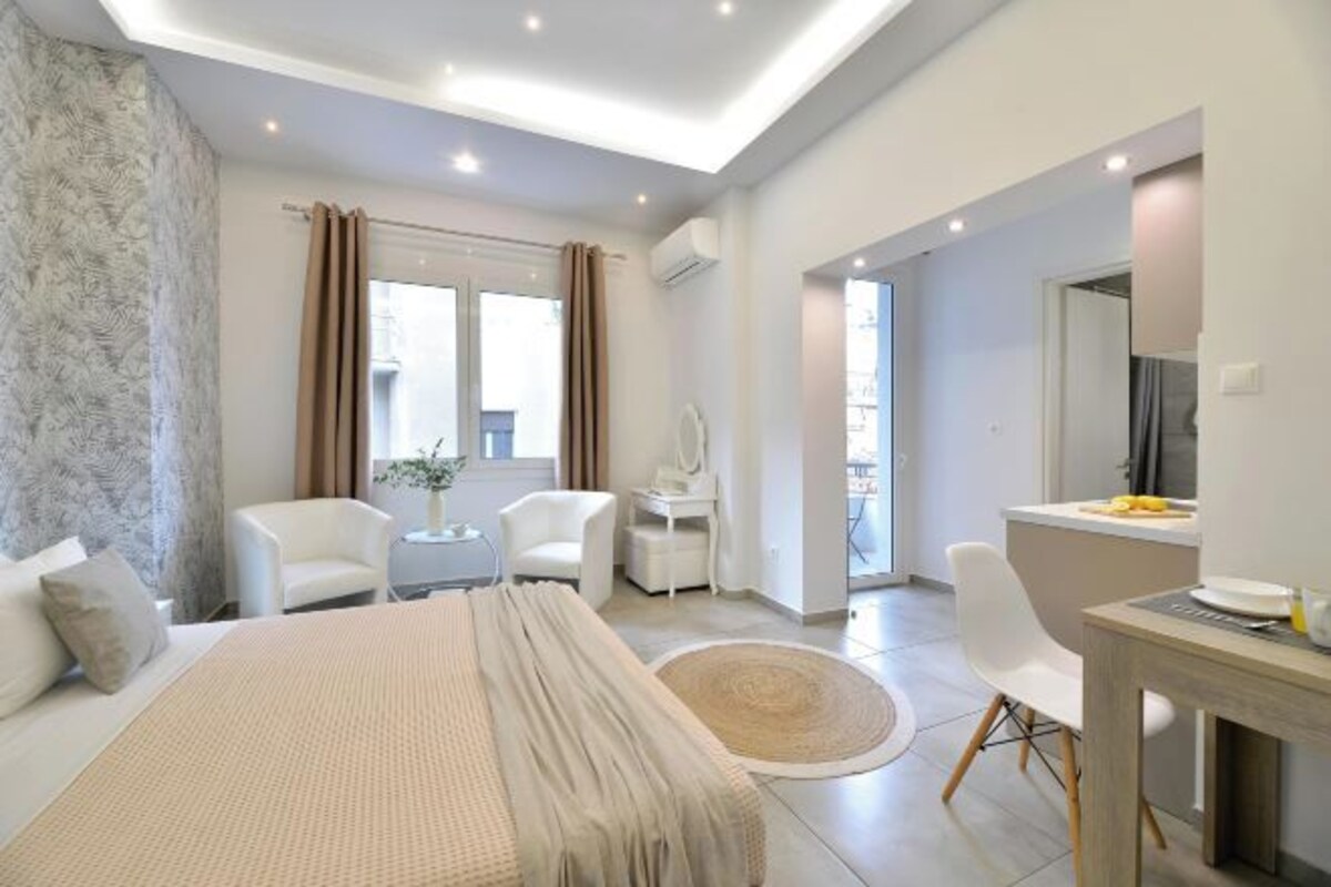 A modern hotel room with a large bed, a desk, a chair, and a small table.