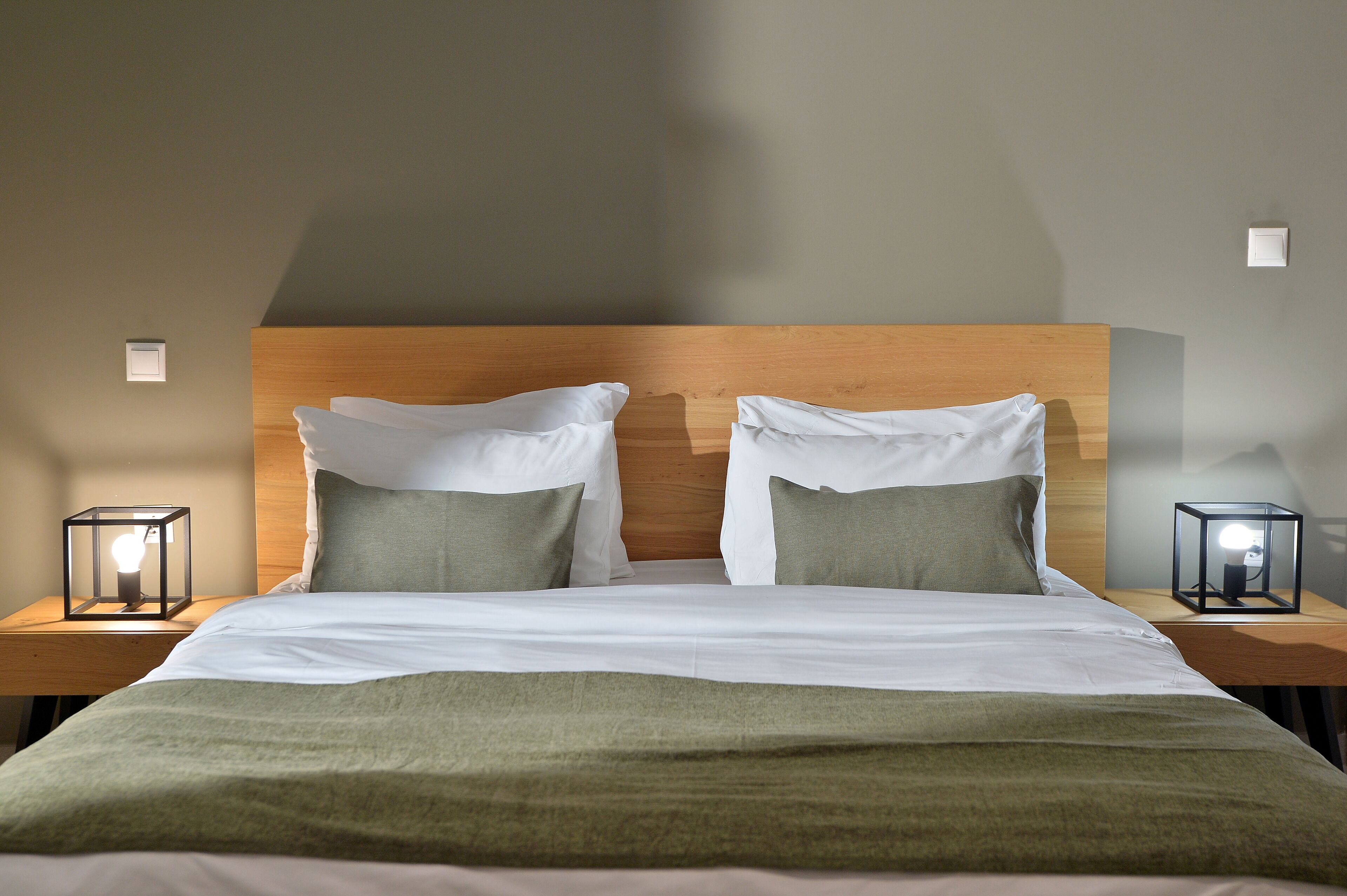 A neatly made double bed with a wooden headboard, two bedside tables with lamps, and a green throw blanket.