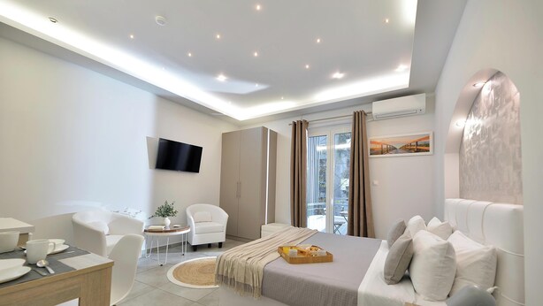 Una moderna camera d'albergo con un letto grande, una scrivania con sedie, una TV e un balcone con tende.