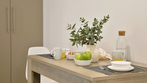 Una tavola imbandita per la colazione con un vaso di foglie verdi, una ciotola di mele, un bicchiere di succo e una bottiglia d'olio.