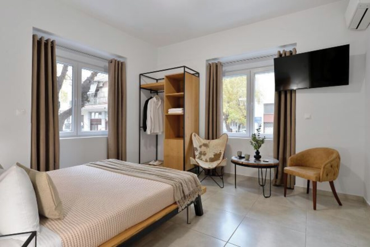 A hotel room with a bed, a seating area with two chairs, a small table, a TV mounted on the wall, and a wardrobe.