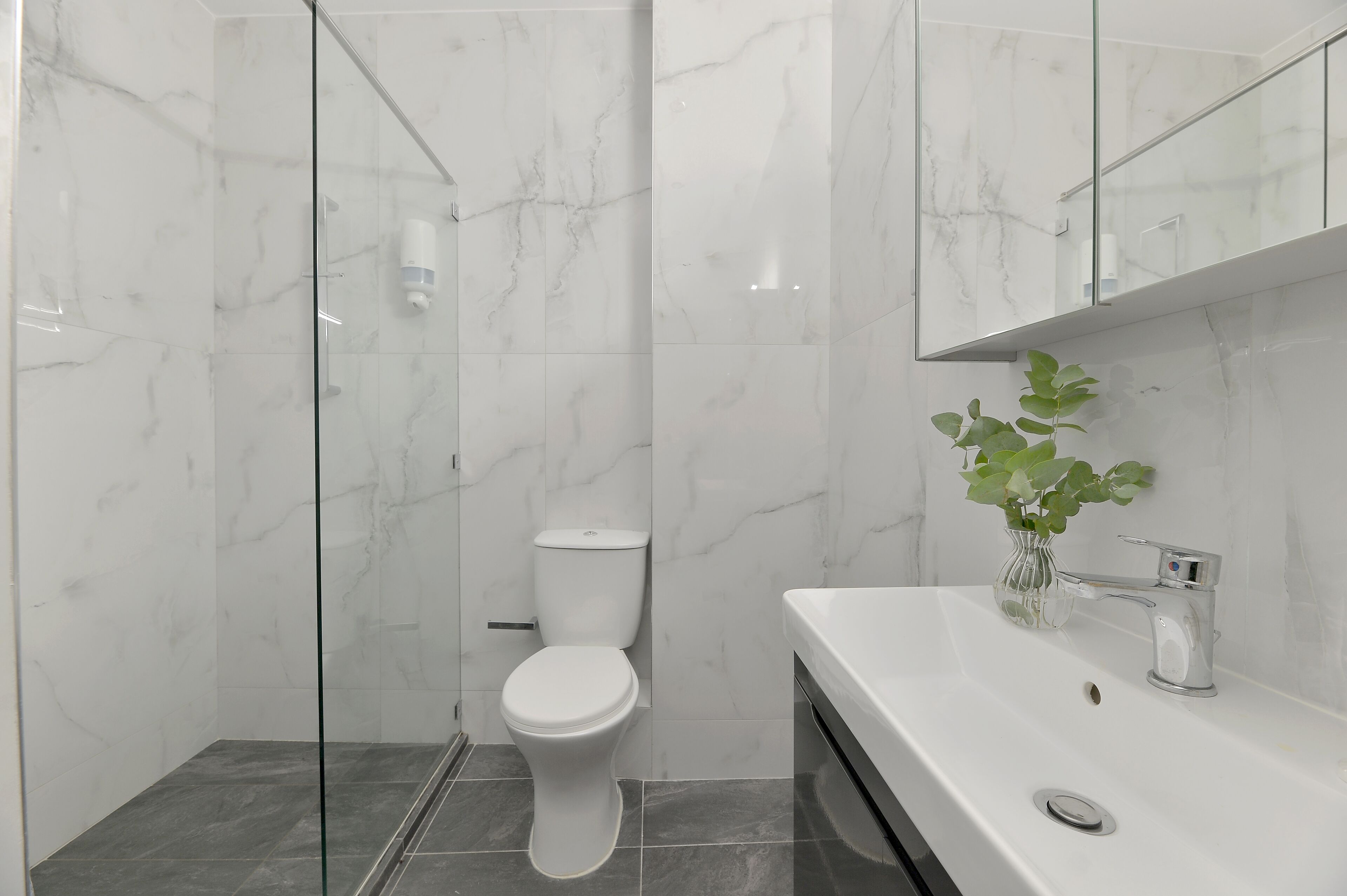 Un baño moderno con cabina de ducha de vidrio, inodoro blanco y lavamanos con espejo.