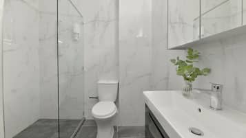 Un baño moderno con cabina de ducha de vidrio, inodoro blanco y lavamanos con espejo.