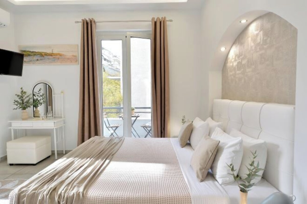 A modern bedroom with a large bed, a white dresser, a flat-screen TV, and a balcony with a view.