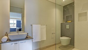 Ein modernes Badezimmer mit einem großen, weißen Waschbecken, einer Duschkabine und einer Toilette.
