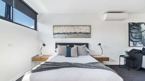 A modern bedroom with a large bed, two bedside tables, a wall-mounted air conditioner, and a large abstract painting above the bed. - Stylish Studio with Great Amenities near Beachside (St Kilda West)