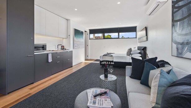 A modern living space with a kitchen, dining area, and a large window offering a view. - Stylish Studio with Great Amenities near Beachside (St Kilda West)