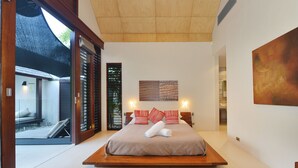 Una camera da letto moderna con un letto grande, una testiera in legno e vista su un giardino tramite una porta scorrevole.