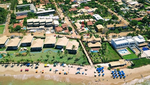 An aerial view of a resort with multiple buildings, a beach with umbrellas, and a pool area. - Excellent house, on the best beach in Itacimirim. (CAMAÇARI)