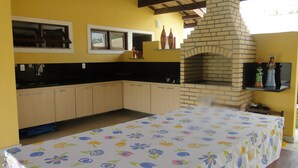 A kitchen with a brick oven, wooden cabinets, a black countertop, and a floral tablecloth. - Excellent house, on the best beach in Itacimirim. (CAMAÇARI)