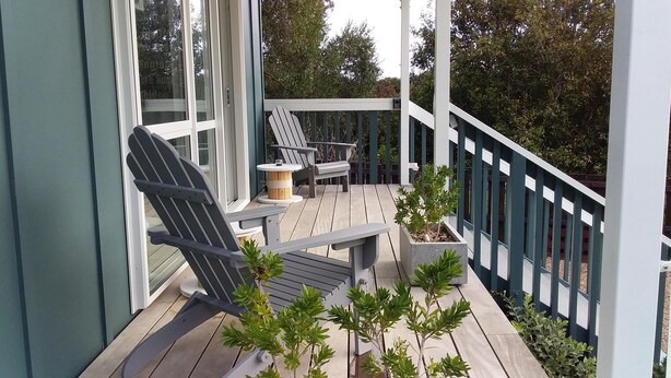 A wooden deck with Adirondack chairs, a small table, and potted plants. - Cute & modern chalet, 500m to sandy beaches, close to vineyards with seaview (Oneroa)