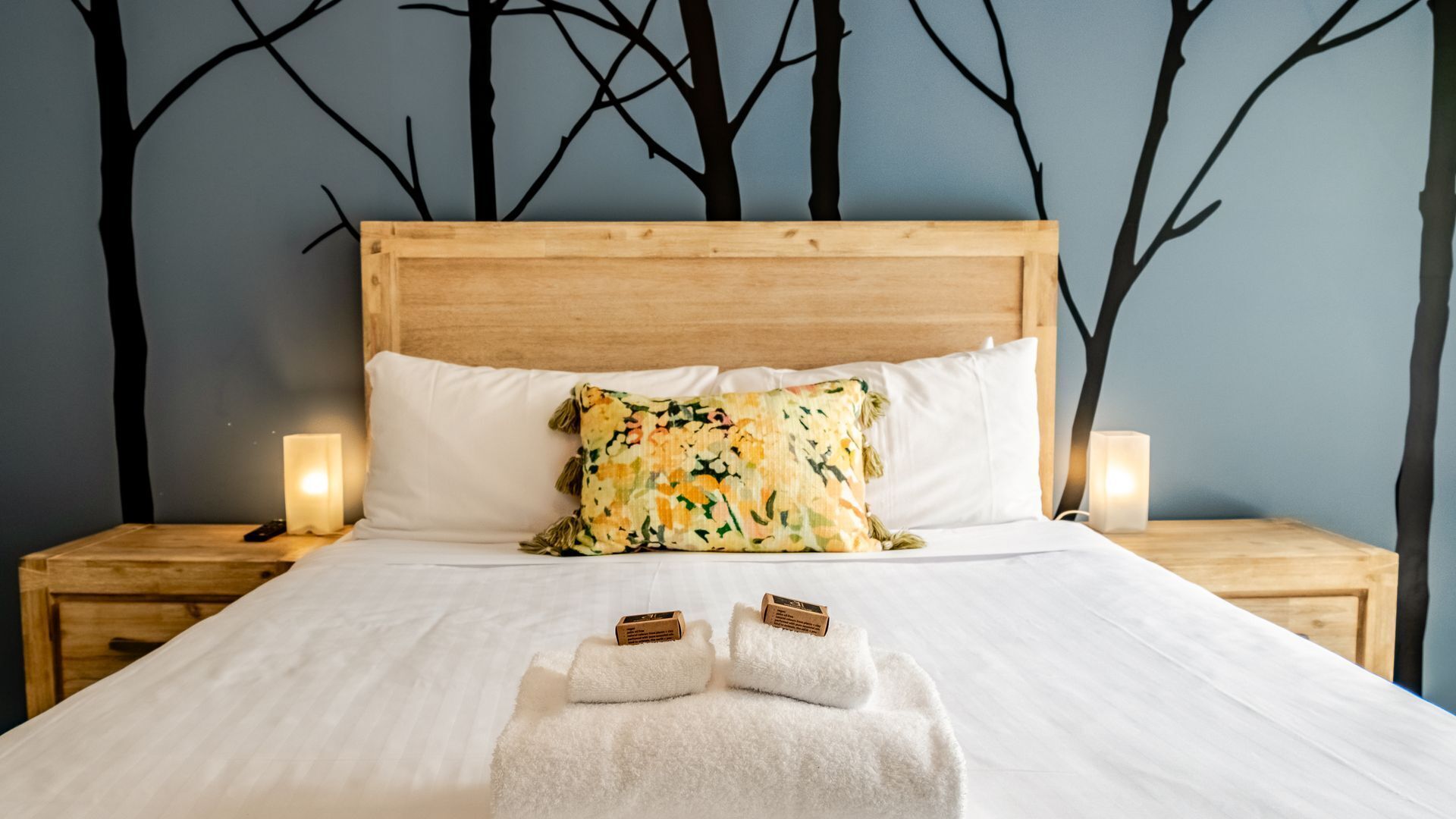 A neatly made bed with white linens, a floral pillow, and two towels on a wooden headboard.