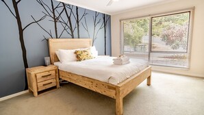 A bedroom with a wooden bed, a nightstand, and a wall mural of trees.