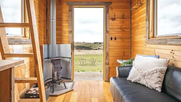 Ein gemütliches Blockhaus-Interieur mit Holzausstattung, Kamin, Sofa und Blick ins Freie.