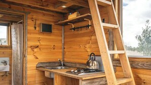 Eine kleine Holzhütte mit Küchenzeile, inklusive Spüle, Herd und einer Klapptreppe.