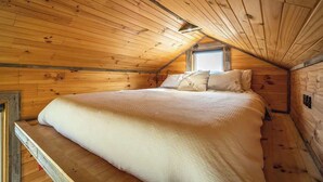 Ein gemütliches Schlafzimmer einer Holzhütte mit einem Einzelbett, einem kleinen Fenster und einer geneigten Decke.