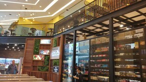 A modern indoor space with a glass display case filled with various packaged goods, a sign reading "PASAR RAYA selections," and a seating area with wooden benches.