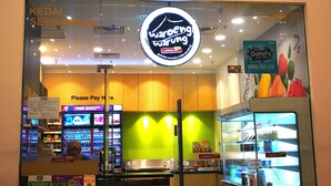 A storefront with a large illuminated sign, a glass entrance, and a display of bottled beverages.