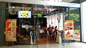 A cafe with a glass facade, outdoor seating, and a sign advertising 'cafe in house' and 'bake in house' services.