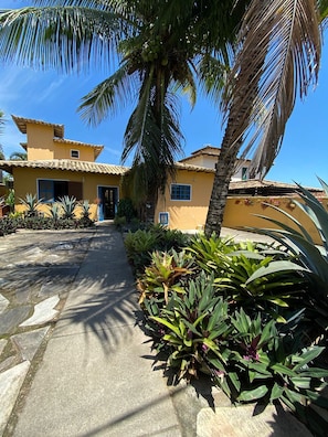 A yellow building with a tiled roof, a paved pathway, and various tropical plants. - offers for low season (Búzios)