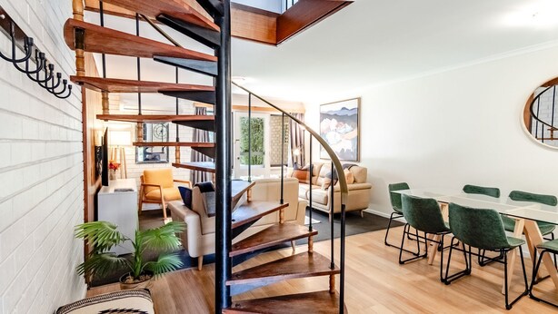 Ein modernes Interieur mit einer Wendeltreppe, einem Essbereich mit grünen Stühlen und einer gemütlichen Sitzecke inklusive Sofa und Sesseln.