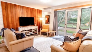 Ein Wohnzimmer mit Fernseher, Sofa, Sessel und einem kleinen Tisch.