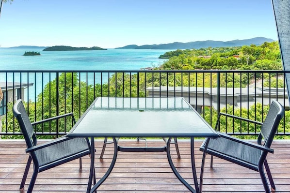 Un balcon avec une table et des chaises donnant sur une étendue d’eau et sur de la verdure.