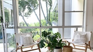 A modern living room with a large glass door leading to a balcony, two wicker chairs, a round coffee table with a woven rug, and a potted plant. - The Nest - 5 minute walk to Hasting Street and Noosa Main Beach (Noosa)