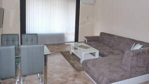 Een woonkamer met een grijze bank, een glazen salontafel en een grijze fauteuil.
