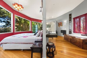 A modern bedroom with a large bed, a vanity, and a view of trees through large windows.